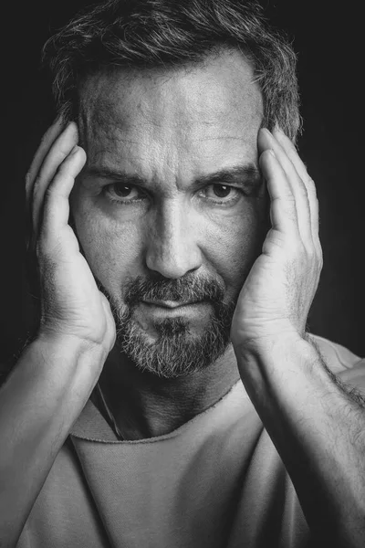 Middle aged grey haired man hold his face with hands looking at camera. Handsome middle aged man in black and white photo. Black and white portrait of attractive, beautiful, serious man — Stock Photo, Image