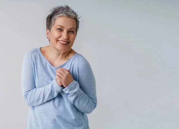 Beautiful mature woman 50s with grey hair posing with hands up next to heart and copy space on right isolated on white background. Copy space and place for product placement. Aged beauty — Fotografia de Stock