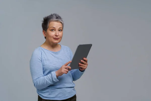 Wanita dewasa yang menakjubkan 50-an berambut abu-abu dengan tablet digital bekerja atau memeriksa di media sosial. Wanita cantik dengan blus biru terisolasi di atas putih. Orang tua dan teknologi. Citra berdada — Stok Foto