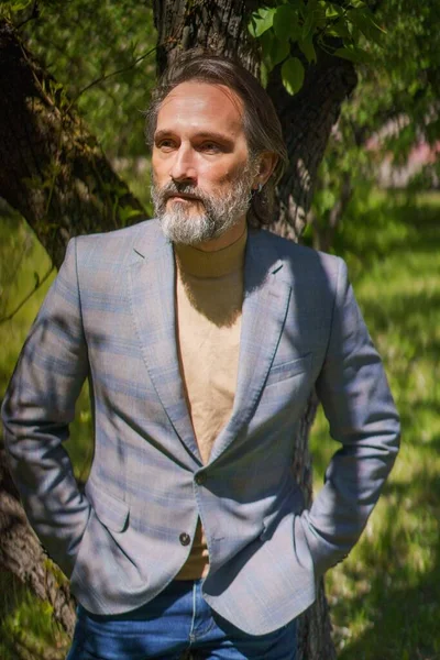 Mature handsome man in 40s 50s in park or yard, away of business or taking a break in warm spring garden outdoors. Handsome grey bearded business man outdoors — Stok Foto