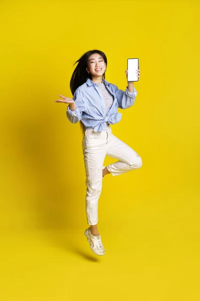 Щаслива Азіатська Дівчина Стрибає Тримаючи Смартфон Показуючи Рекламу Мобільного Додатку — стокове фото