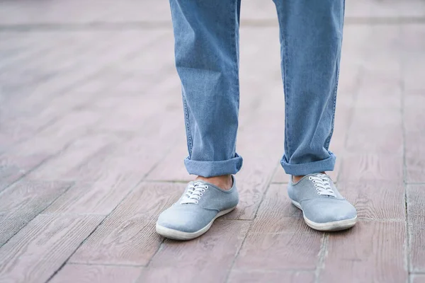 Stylish man feet in denim jeans and sneakers shoes standing alone outdoors on street marble or ceramic plate.