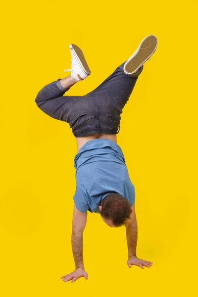 Up side down young man in casual wear standing back on camera posing on yellow background. Stylish gymnast guy working out in studio. Athletic young man walking on hands on yellow background.