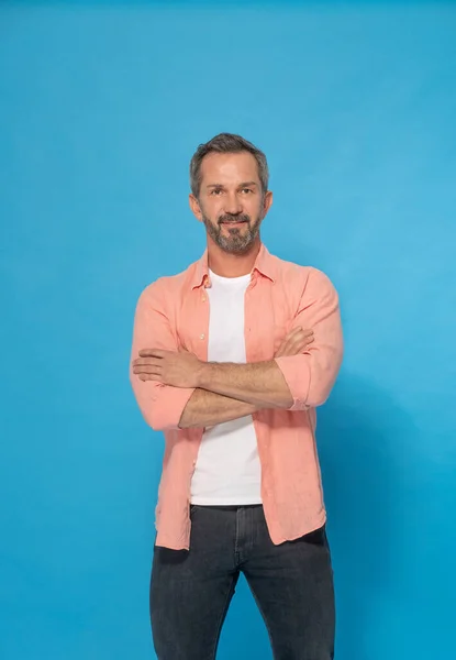 Strong handsome middle aged man with grey beard 40s, 50s wearing casual isolated on blue background. Smiling mature muscular, fit, athletic man posing in studio. Mature fit man health and physics.