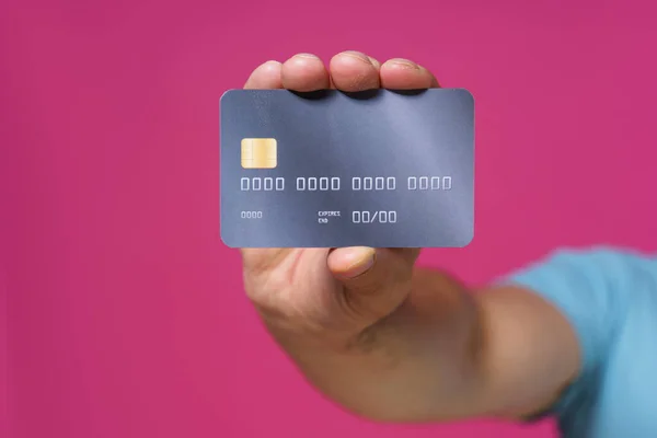 Dark grey-purple debit, credit card in man hand isolated on pink background. Financial, banking concept. No face visible.