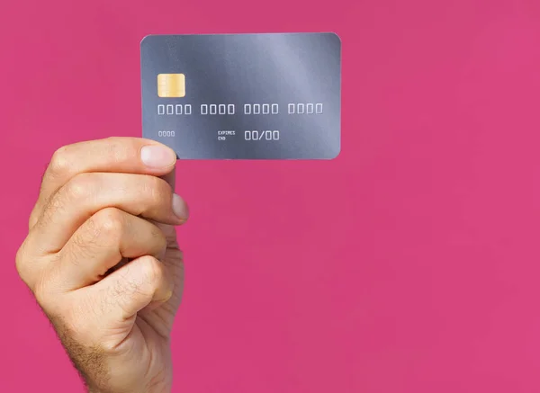 Great offer. Dark grey-purple debit, credit card in man hand isolated on pink background. Financial, banking concept. No face visible.