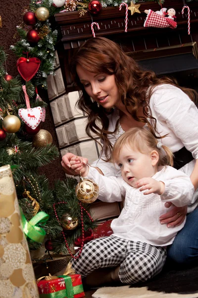 Feliz madre decorando el árbol de Navidad con su bebé Imágenes De Stock Sin Royalties Gratis