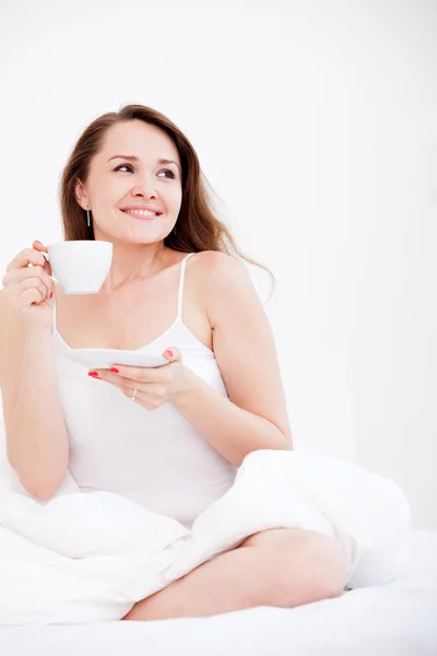 Frau sitzt auf einem Bett mit einer Tasse — Stockfoto