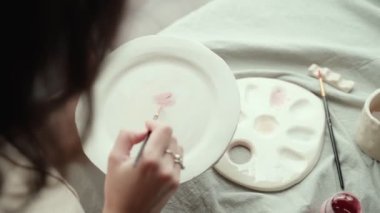 Ekin ustası kadın bulaşık takımlarına pembe boya sürüyor.