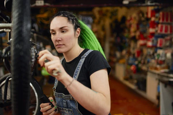 Serious woman fixing wheel of bicycle in repair shop — Stock Photo, Image