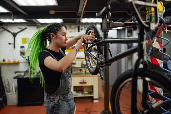 Gayri resmi bir kadın atölyede bisiklet tamir ediyor. — Stok fotoğraf