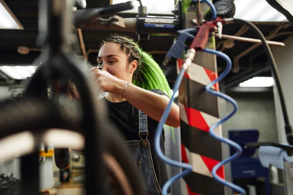 Positieve jonge vrouwelijke monteur controleren fiets in garage — Stockfoto