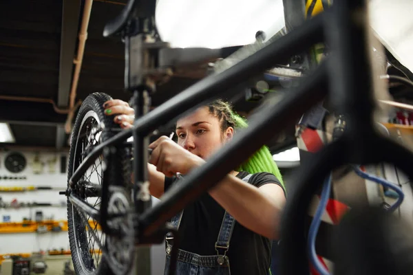 Serieuze vrouwelijke master schroeven fietswiel in werkplaats — Stockfoto