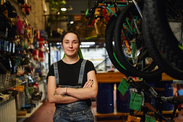 Bisikletçi dükkanında kollarını kavuşturmuş arkadaş canlısı bir bayan. — Stok fotoğraf