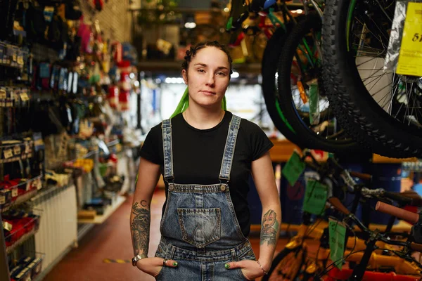 Tattooed woman standing in store with hands in pockets — Stock Photo, Image