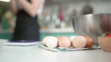 Ekin kadın mutfakta yumurta ve kase ile masada duruyor.