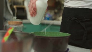 Mahsul kadın mutfaktaki tencereye süt döküyor.