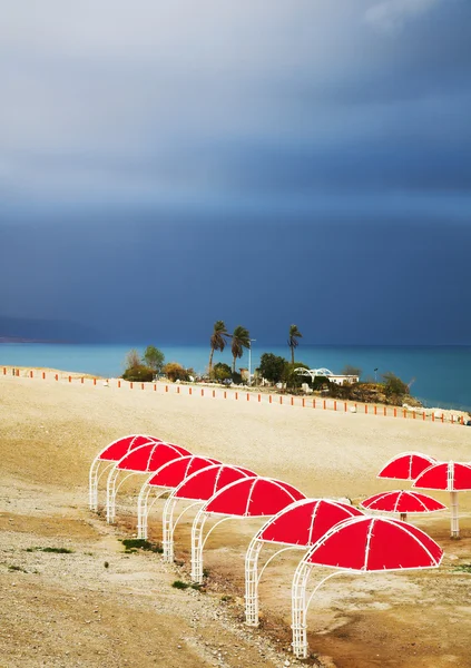 Röd parasoller på kusten av döda havet i thunder-storm — Stockfoto