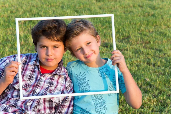两个可爱的男孩笑着 透过一个白色的框架看着观众 绿色夏季草坪 肖像和广告照片 — 图库照片