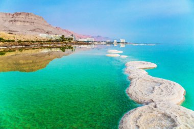 İsrail. Sabahın erken saatlerinde Ölü Deniz 'in tatil köylerinde. Gök mavisi deniz suyu iyileştirici tuzlarla doludur. Küçük adacıklar ve sudaki tuz yolu. Ekolojik, tıbbi ve fotoğraf turizmi kavramı