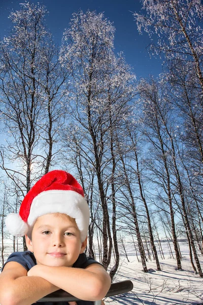 クリスマスが来る 冬の森の中で霜の多い雪の晴れた日 深い雪が地面を覆っていた ハンサムな男の子で赤サンタクロースの帽子の笑顔 — ストック写真