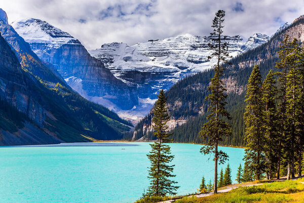Beautiful sunny fine day. Glacial Lake Louise in Banff Park, Canadian Rockies. The lake with azure water is surrounded by mountains and forests. The concept of ecological, active and photo tourism