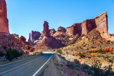 Asfalt yolu. Resimli kırmızı-kahverengi kumtaşı kayalıkları eşsiz bir manzara oluşturur. Arches Park 'ın eşsiz güzelliği. Görkemli kayalar doğal kaynaklıdır. Utah, ABD 'deki Arches Park. 