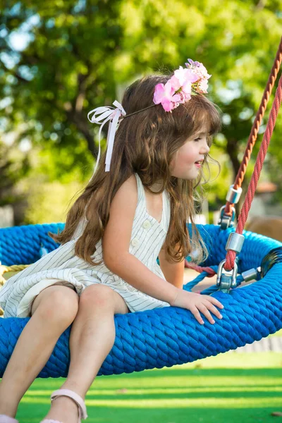 長い髪の毛に花の花輪で魅力的な女の子は子供のスイングで陽気に笑顔 子供公園の暖かい夏の日 — ストック写真