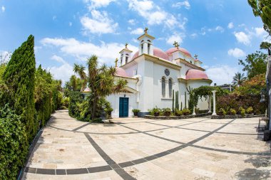 Kilisenin etrafındaki tropik park. Galilee Denizi kıyılarındaki manastırın altın haçlarıyla dolu pembe kubbeler. Capernaum 'daki On İki Havarinin Yunan Ortodoks Manastırı. 
