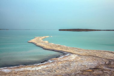 Aktif ve fotoğraf turizmi kavramı. İsrail. Ölü Deniz üzerinde loş kış günü. Gökyüzü ufukta denizle birleşir. Suyun üzerinde buharlaşmış tuz çıkıntıları