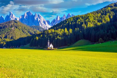 Majestic Dolomites. Small white church with a bell among green lawns on the sunset. Tyrol, Italy. The village Santa Maddalena in the Val di Funes Valley. The concept of ecological and photo tourism