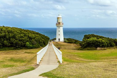 The path to the lighthouse is fenced with a railing. Magnificent snow-white lighthouse on the ocean shore. The Great Ocean Road runs along the Pacific coast of Australia 