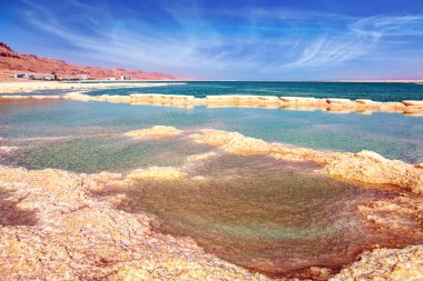 The evaporated salt forms bizarre patterns on the surface of the water. The Israeli coast of the Dead Sea. Windy spring day. Cirrus clouds fly in the blue sky