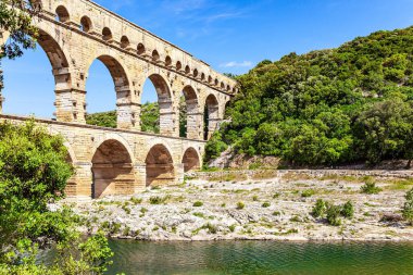  The Pont du Gard is the tallest Roman aqueduct. The aqueduct  Pont du Gard is a three-tiered arcade of yellow-pinkish limestone. The shallow Gardon River.