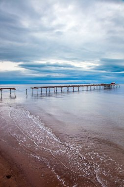 Ruined ocean pier in Punta Arenas. Strait of Magellan. South America. The famous Tierra del Fuego is visible on the horizon. The sky is covered with heavy thunderclouds