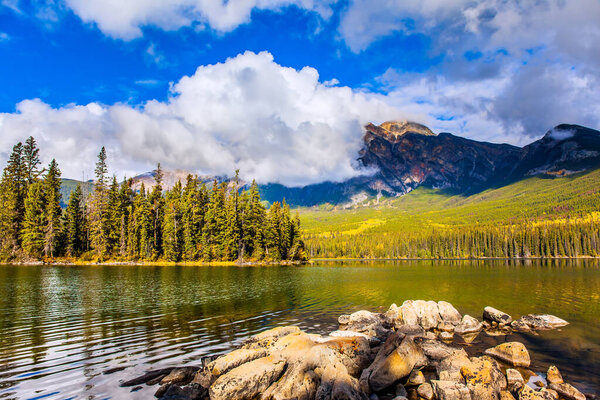 Пирамидное озеро. Гора Пирамида покрыта кучевыми облаками. Озеро покрыто легкой водяной рябью. Холодный солнечный день в Скалистых горах Канады. 