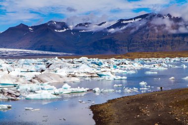  İzlanda. Skaftafell Parkı. Jokulsaurloun gölü. Göl dağlarla çevrilidir. Suya yansıyan beyaz ve mavi buzdağları ve buz kütleleri. Kuzey ve fotoğraf turnuvaları konsepti