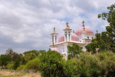 Pembe kubbeler ve Galilee Denizi kıyılarındaki manastırın kar beyazı duvarları. Kilisenin etrafındaki tropik park. Capernaum 'daki On İki Havarinin Yunan Ortodoks Manastırı.
