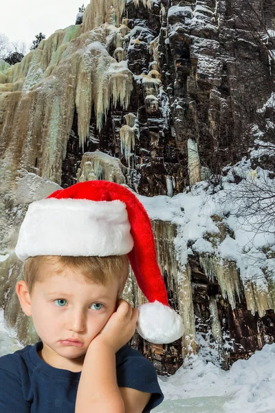 ラップランドの新年 サンタクロースへの旅 険しい崖の上に多色の氷のストリーム 赤いサンタクロースの帽子に青い目の悲しい少年 生態観光と写真観光の概念 — ストック写真