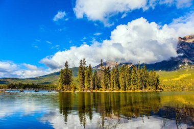 Kanada 'nın Rocky Dağları' nda soğuk güneşli bir gün. Piramit Gölü. Pürüzsüz, soğuk su gökyüzünü ve bereketli kümülüs bulutlarını yansıtır. Etkin eko ve fotoğraf turizmi kavramı