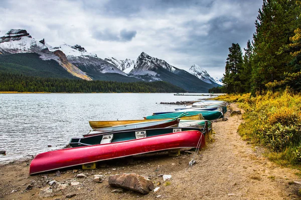 カナダのロッキー山脈で寒い曇りの日 雪の中で湖マレーニュ帽をかぶった山々針葉樹常緑樹林に囲まれています 湖畔で乾燥した多色のボートやカヌー — ストック写真