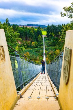 Muhteşem Geyerlei Almanya 'daki en uzun asma kablo köprüdür. Rüzgarlı ve soğuk bir sonbahar günü profesyonel kameralı bir kadın güzel bir manzaranın fotoğraflarını çeker.. 