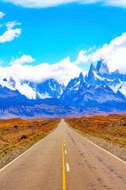 Fitzroy Dağı 'na giden yol. Meşhur en tepedeki kaya tekelleri güneş tarafından aydınlatılır. Arjantin Patagonya 'sı. Sonsuz düzlükler sarı sonbahar otlarıyla kaplıdır.