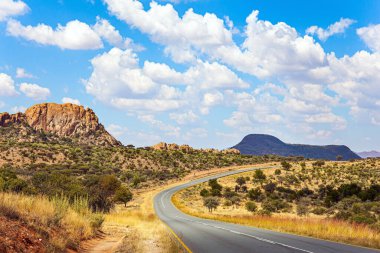 Paved otoyolu düz savanayı geçer. Sıcak bir gün, yemyeşil bulutlar mavi gökyüzünde süzülüyor. Afrika 'ya git. Namibya 'daki sihirli çöl. 
