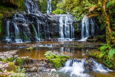 New Zealand, South Island. Picturesque multi-tiered cascading waterfalls among the green forest. Purakaunui Falls. The concept of active, environmental and photo tourism