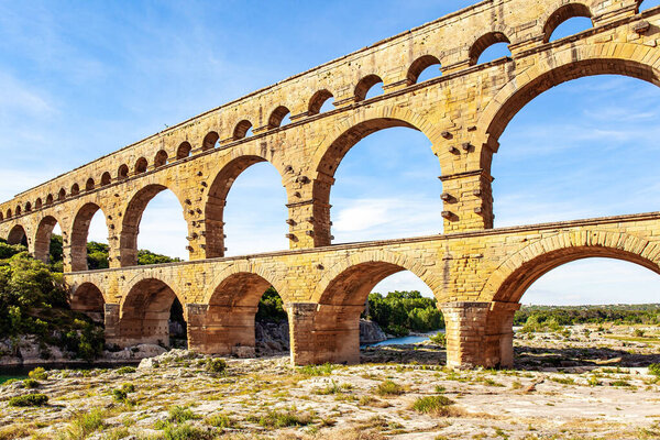 The Pont du Gard is the tallest Roman aqueduct. Picturesque antique aqueduct. The shallow Gardon River in a bright sunny day. Interesting trip to France. 