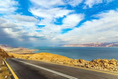 Doğanın mucizesi - Ölü Deniz. Otoyol Ölü Deniz kıyısı boyunca uzanıyor. Bulutlu ve sıcak Ocak günü. İsrail. Denizin karşı kıyısındaki Ürdün loş kış güneşiyle aydınlanır.