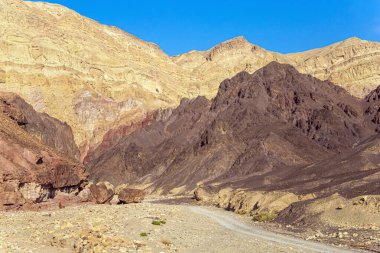 Sıcak Kasım günü. Taş çölün geçidinde toprak yol. Eilat Dağları. Renkli peyzaj oluşumları. İsrail dağlarında yıpranmış kumtaşının garip şekilleri