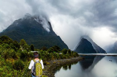 Yeşil sırt çantalı kadın yoldaymış. Okyanus fiyordu Milford Sound. Yeni Zelanda. Egzotik, ekolojik ve fotografik turlar kavramı