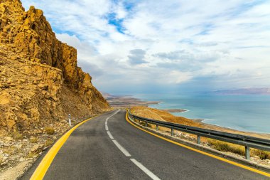 İsrail. Otoyol Ölü Deniz kıyısı boyunca uzanıyor. Denizin karşı kıyısındaki Ürdün loş kış güneşiyle aydınlanır. Bulutlu Ocak günü. Deniz yüzeyi bulutları yansıtır..